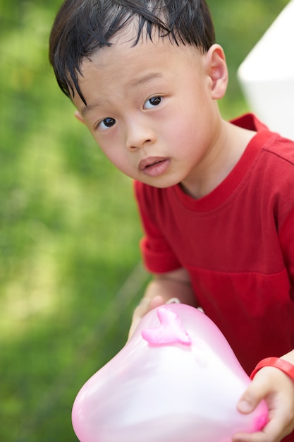 Śliczny Azjatykci Chłopiec Chwyta Menchii Serce Kształtował Balon Na Trawa Jarda Ogródu Plecy Ziemi