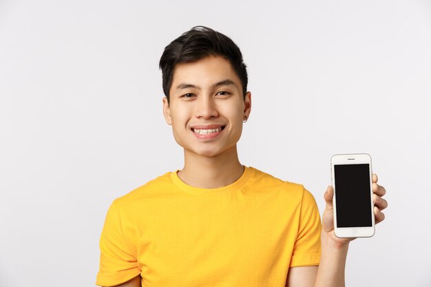 Śliczny azjatykci mężczyzna w żółtej koszulce pokazuje smartphone