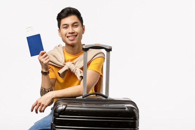Śliczny azjatykci mężczyzna w żółtej koszulce przygotowywającej dla podróży trzyma paszport