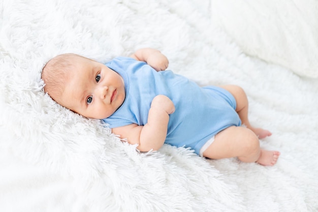 Śliczny chłopczyk w wieku trzech miesięcy w niebieskim body na białym łóżku w domu