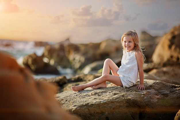 Śliczny małej dziewczynki obsiadanie na plaży przy zmierzchem