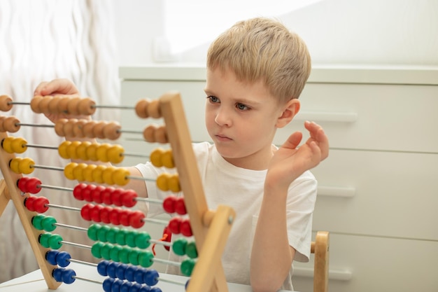 Śliczny mały chłopiec blondynka jest zajęty kolorowymi drewnianymi rachunkami dla dzieci. Gry Montessori. Edukacja koncepcyjna.