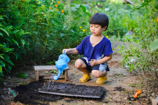 Śliczny mały chłopiec podlewa rośliny konewką w ogrodzie