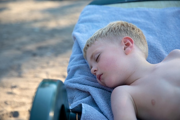 Śliczny mały chłopiec śpi na leżaku na ręczniku na plaży Koncepcja letnie wakacje z dzieciństwa