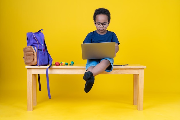 Śliczny mały chłopiec uczący się Internetu lub grający w gry na swoim laptopie