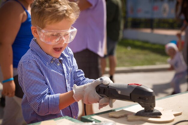 Śliczny mały chłopiec w plastikowych bezpiecznych okularach szlifuje drewnianą deskę na zewnątrz
