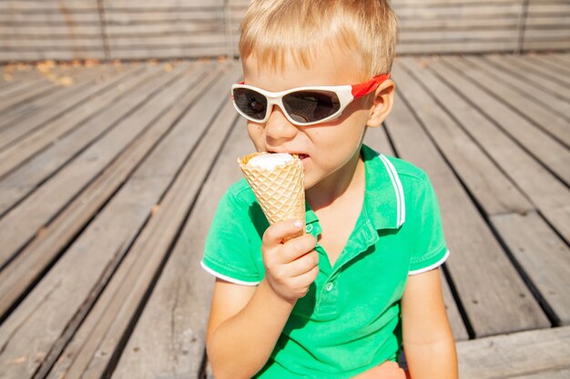 Śliczny mały dzieciak w okularach przeciwsłonecznych jedzący lody