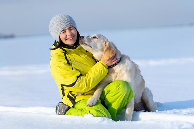 Śliczny młody pies retriever całuje roześmianą kobietę na zaśnieżonym polu