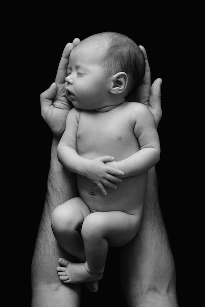 Zdjęcie Śliczny noworodek w rękach ojca na czarnej ścianie