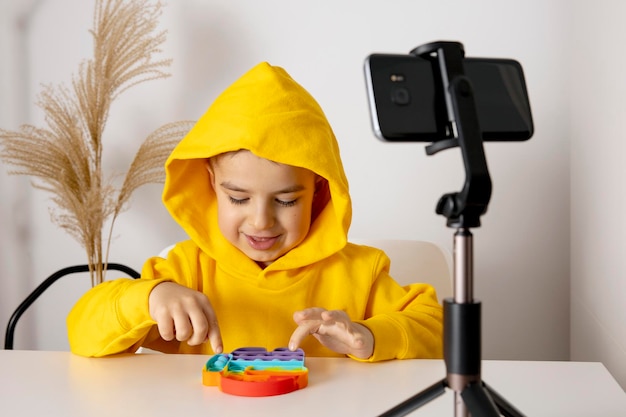 Śliczny, słodki mały chłopiec bloger nagrywający blog dotyczący stylu życia rozmawiający z kamerą smartfona na statywie Młody influencer filmujący vlog na swoim kanale Dziecko nagrywa wideo dla swoich obserwatorów online