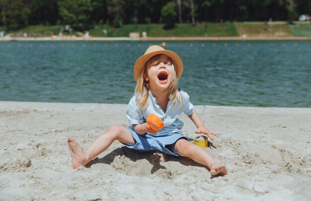 Śliczny szczęśliwy blond chłopiec bawi się zabawkami plażowymi na piaszczystej plaży miejskiej