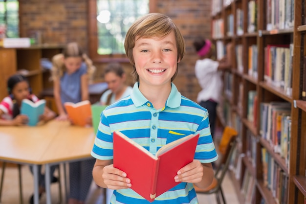 Śliczny uczeń ono uśmiecha się przy kamerą w bibliotece