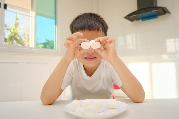 Śliczny zabawny mały azjatycki chłopiec siedzi w kuchni z pianką w domu niezdrowe przekąski dla dzieci