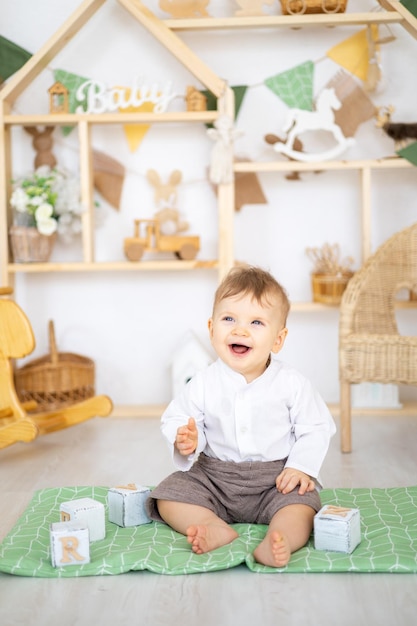 Śliczny zdrowy chłopiec bawi się drewnianymi zabawkami edukacyjnymi w jasnym przytulnym pokoju dziecięcym w domu na tle drewnianego domu