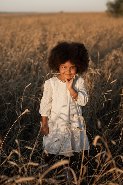 Słodka afrykańska dziewczyna w białej sukience z puszystą fryzurą idąca po letnim polu o zachodzie słońca
