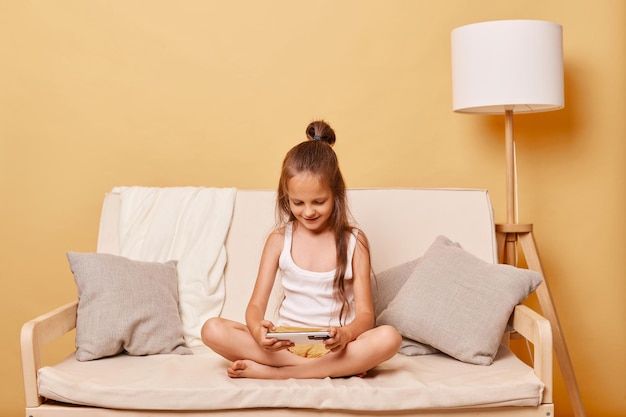 Słodka brązowa dziewczynka oglądająca kreskówki na telefonie, grająca w gry wideo online, nosząca zwykłe ubrania domowe, spędzająca wolny czas w Internecie.