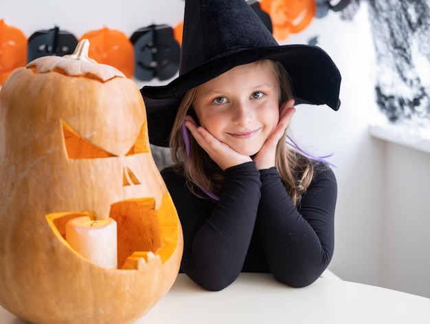 Słodka dziewczyna w kostiumie czarownicy z dynią w domu bawi się świętując Halloween