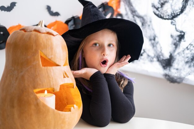 Słodka dziewczyna w kostiumie czarownicy z dynią w domu bawi się świętując Halloween