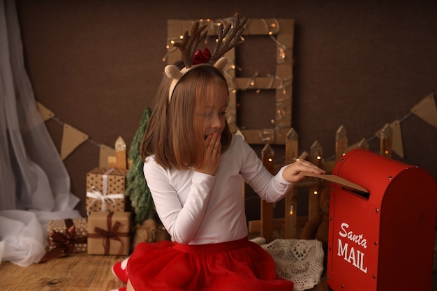 Słodka dziewczyna w stroju noworocznym wrzuca do skrzynki list do Świętego Mikołaja