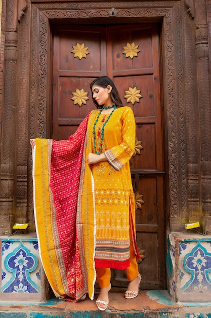 Słodka dziewczyna w tradycyjnej sukience Desi do sesji zdjęciowej przed starymi drewnianymi drzwiami