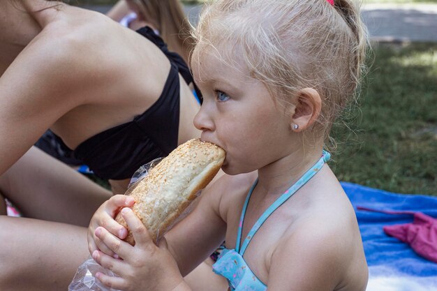Słodka dziewczynka jedząca bułkę w parku miejskim