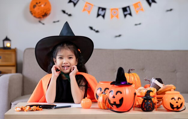 Słodka dziewczynka ubrana w kostium na Halloween siedzi na sofie i szczęśliwie patrzy w kamerę