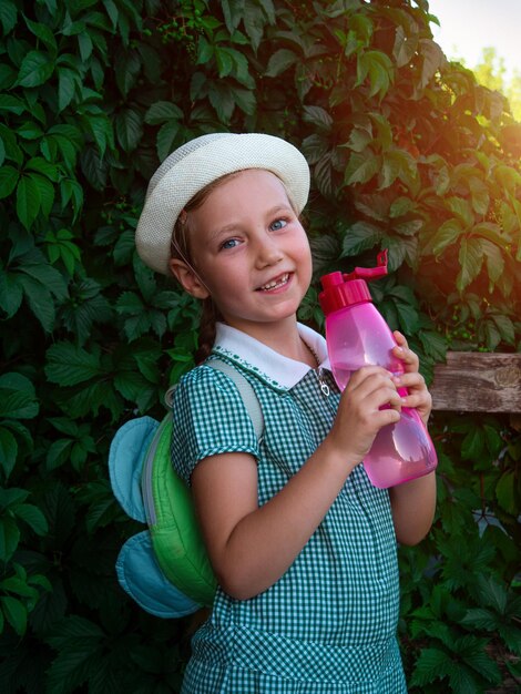 Słodka dziewczynka ze szkoły pije wodę z różowej butelki na świeżym powietrzu. Dziecko cieszy się świeżą, zimną wodą.