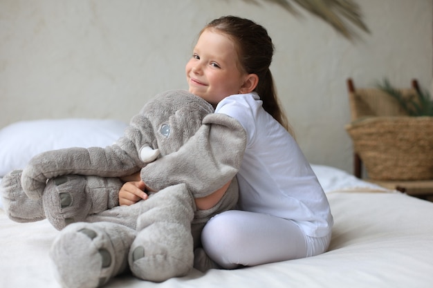 Słodka mała dziewczynka siedzi na łóżku w domu ze słonikiem.