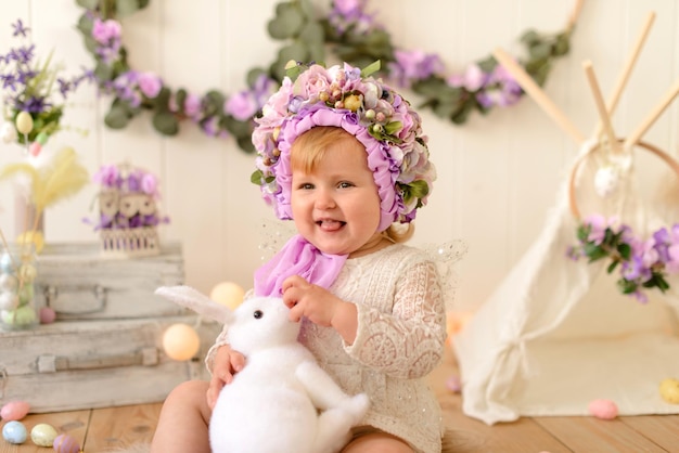 Słodka mała dziewczynka z dekoracją na głowie i kolorowymi jajkami wielkanocnymi na białym drewnianym tle