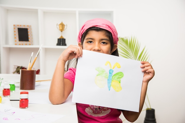 Słodka mała indyjska lub azjatycka dziewczynka lubi rysować lub malować pędzlem i malować na papierze w domu