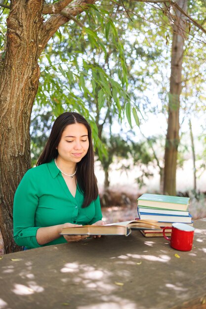 Słodka młoda kobieta czytająca książki na polu pod wierzbą z kubkiem do kawy Światowy dzień książki