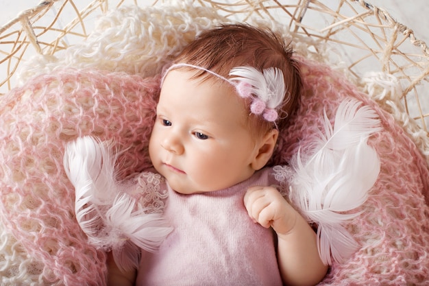 Zdjęcie słodka nowonarodzona dziewczynka z otwartymi oczami. nowonarodzona dziewczynka w wieku 3 tygodni leżąca w koszu z dzianinową kratą. portret dziewczyny całkiem noworodka. obraz zbliżenie