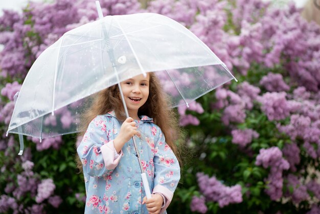 Słodka pięcioletnia dziewczyna z przezroczystym parasolem na tle kwitnących bzów