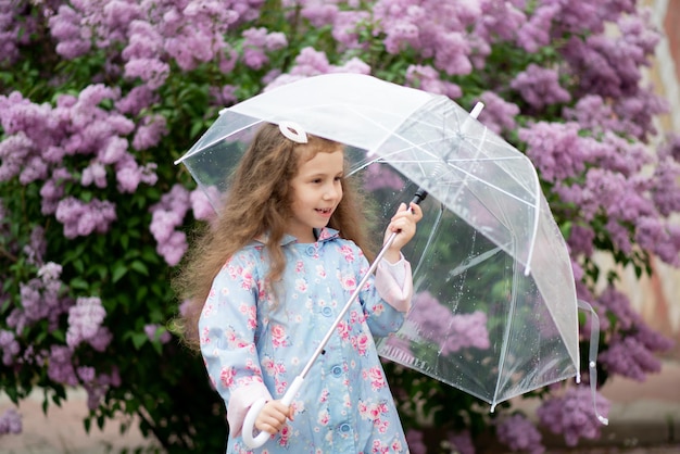 Słodka pięcioletnia dziewczyna z przezroczystym parasolem na tle kwitnących bzów