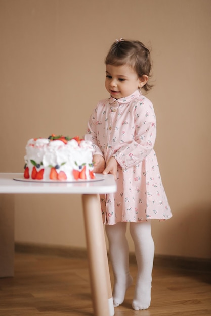 Słodka półtoraroczna dziewczynka stoi obok pysznego tortu urodzinowego Osiemnastomiesięczna dziewczynka jest bardzo szczęśliwa i śmieje się Jedzenie wegetariańskie Bez laktozy i glutenu