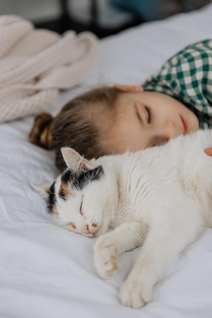 Słodka sześcioletnia dziewczynka zasnęła słodko obok puszystego kota na swoim łóżku Dziecko z kotem śpi na białym łóżku