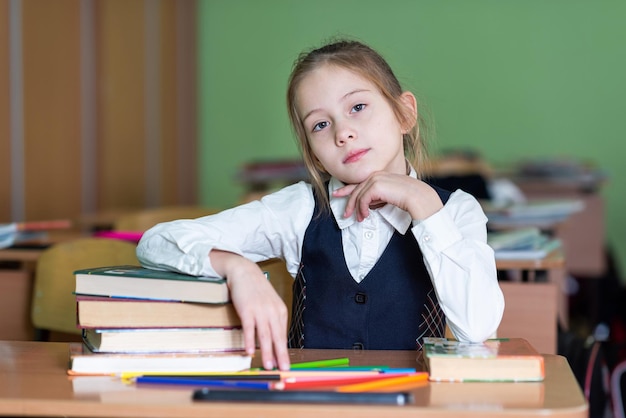 Słodka Uczennica Siedzi Przy Biurku Otoczona Książkami Spogląda W Kamerę Szkolne życie