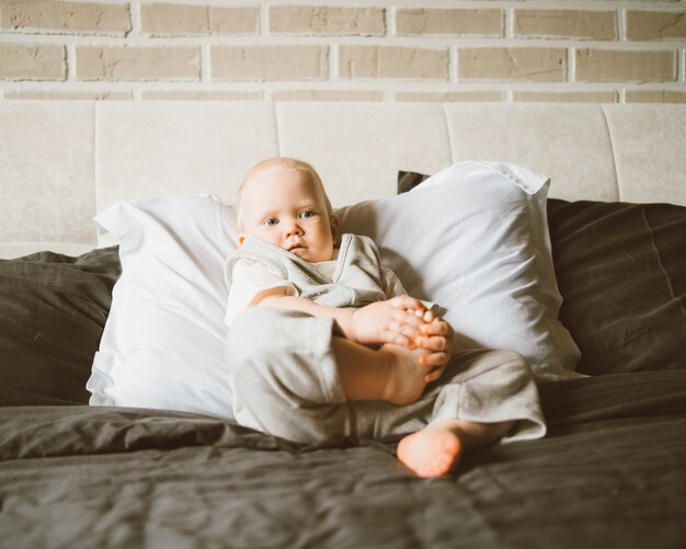 Zdjęcie słodki chłopczyk bawi się stopami leżąc na dużym łóżku w domu