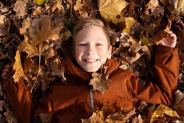 Słodki chłopiec leży w suchych jesiennych liściach i uśmiecha się