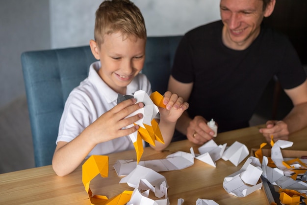 Zdjęcie słodki chłopiec siedzi ze swoim tatą przy stole i zbiera origami przyklej części
