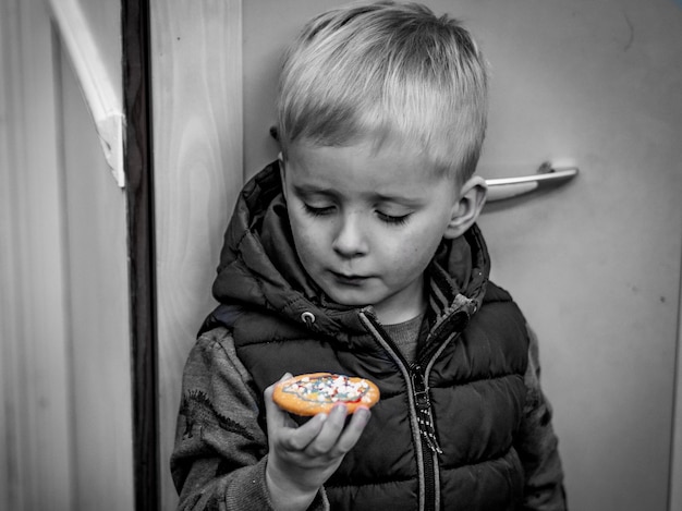 Słodki chłopiec trzymający ciasteczko, stojąc przy drzwiach w domu.