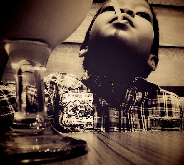 Zdjęcie słodki chłopiec z słomą w ustach patrzący w górę siedząc na stole w restauracji