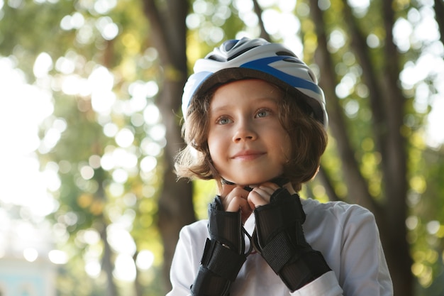 Słodki chłopiec zakłada kask ochronny do jazdy na łyżwach w parku