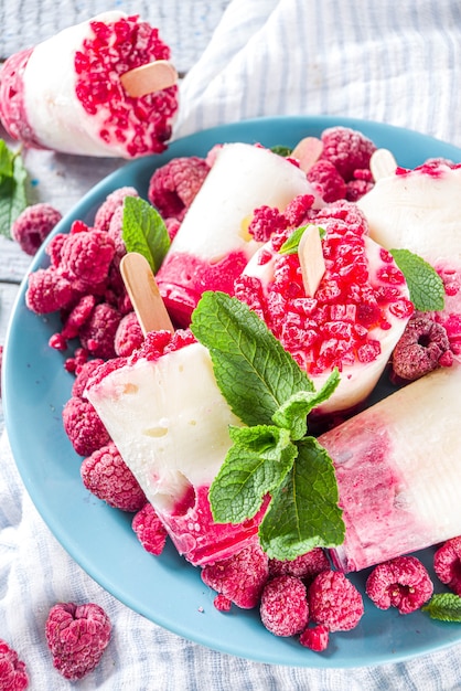 Słodki i smaczny letni deser dietetyczny. Domowy jogurt malinowy ze świeżymi malinami i miętą. Przepis na zdrowe lody. Drewniane białe tło kopii przestrzeni