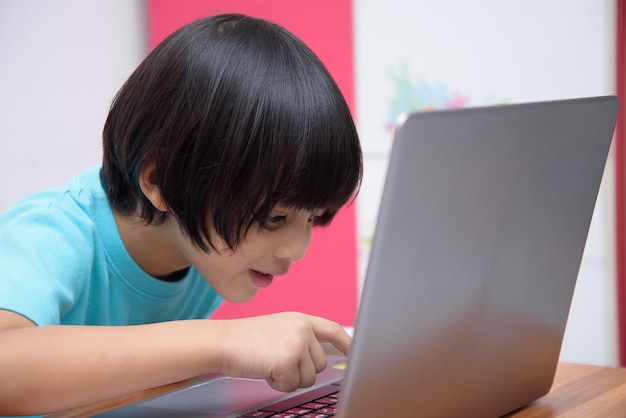 Słodki, inteligentny azjatycki chłopiec z radością używa swojego laptopa do samodzielnej nauki online w domu Koncepcja uczenia się online Samodzielna nauka