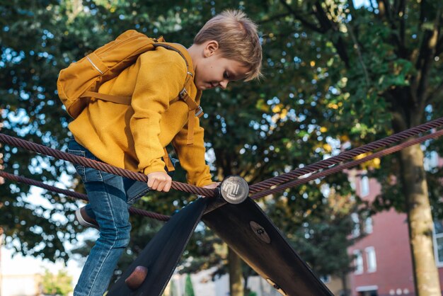 Zdjęcie słodki mały chłopiec bawi się na placu zabaw chłopiec wspina się na ramę wspinaczkową parki miejskie