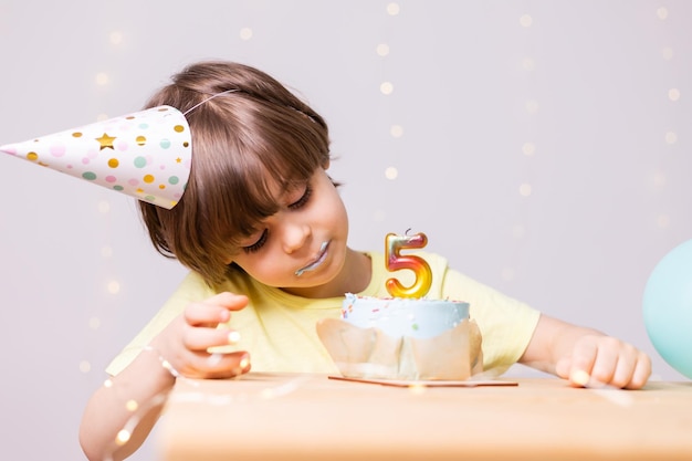 słodki mały chłopiec urodzinowy je tort w kapeluszu balony z okazji urodzin