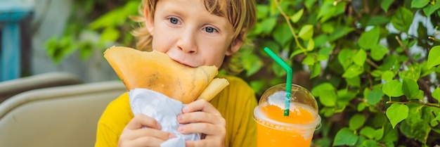 Słodki mały kaukaski chłopiec je naleśniki i pije sok pomarańczowy w długim formacie