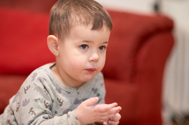 Zdjęcie słodki młody chłopiec jedzący ser w domu podczas oglądania telewizji obok kanapy osoby