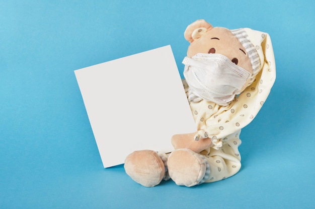 Słodki pluszowy niedźwiedź w masce na twarzy trzyma pocztówkę na niebieskim tle na miejsce do kopiowania tekstu